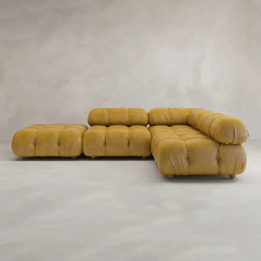 The Belmont Sofa Combination C is a modular mustard yellow leather sectional with marshmallow-like curves, tufted rounded cushions, and low backrests—an iconic classic in modern design—set against a textured neutral wall on a light gray floor.