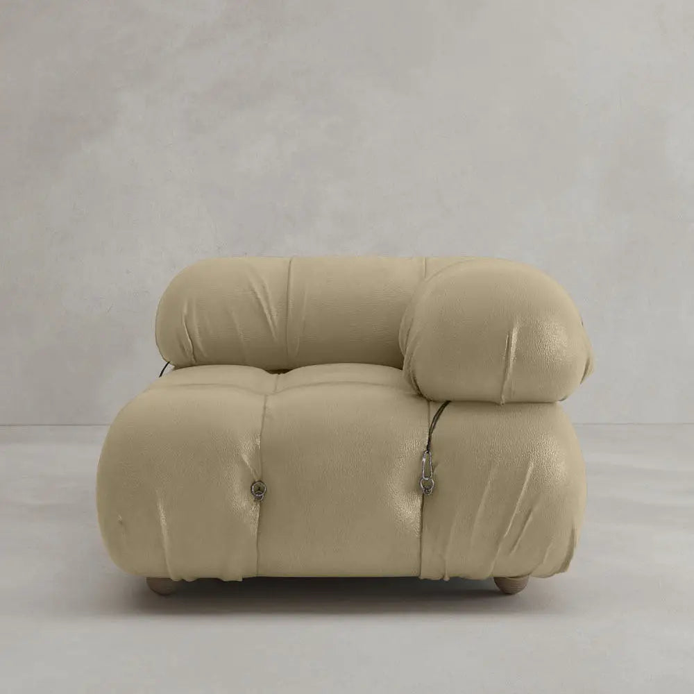 The Belmont Sofa Left Armrest features modern, plush beige upholstery with soft, rounded cushions and button detailing, set against a light gray textured wall and floor—perfect for any modular design aesthetic.