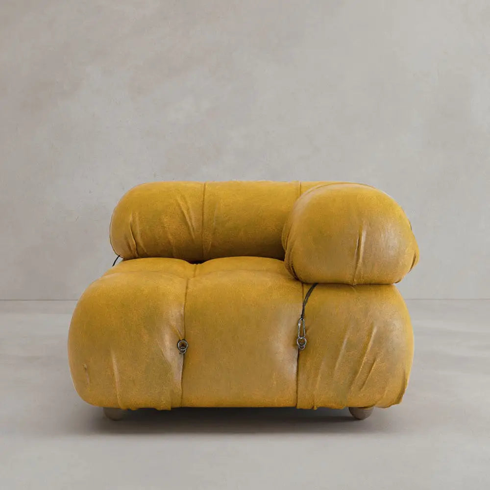 The Belmont Sofa Left Armrest, in plush mustard yellow with a rounded tufted design and visible black fasteners, evokes iconic classic style against a plain light grey wall and floor.