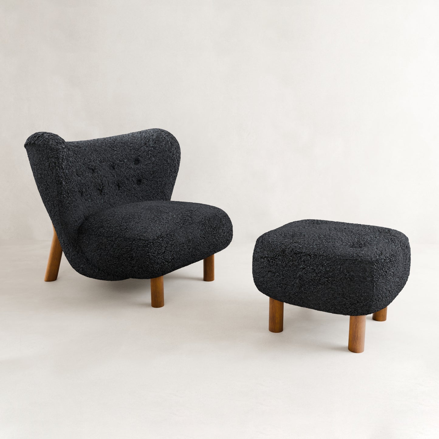 The Highgate Chair With Ottoman features modern curved lines, textured dark gray vegan shearling upholstery, and wooden legs—set against a plain light backdrop for a bold contemporary statement.