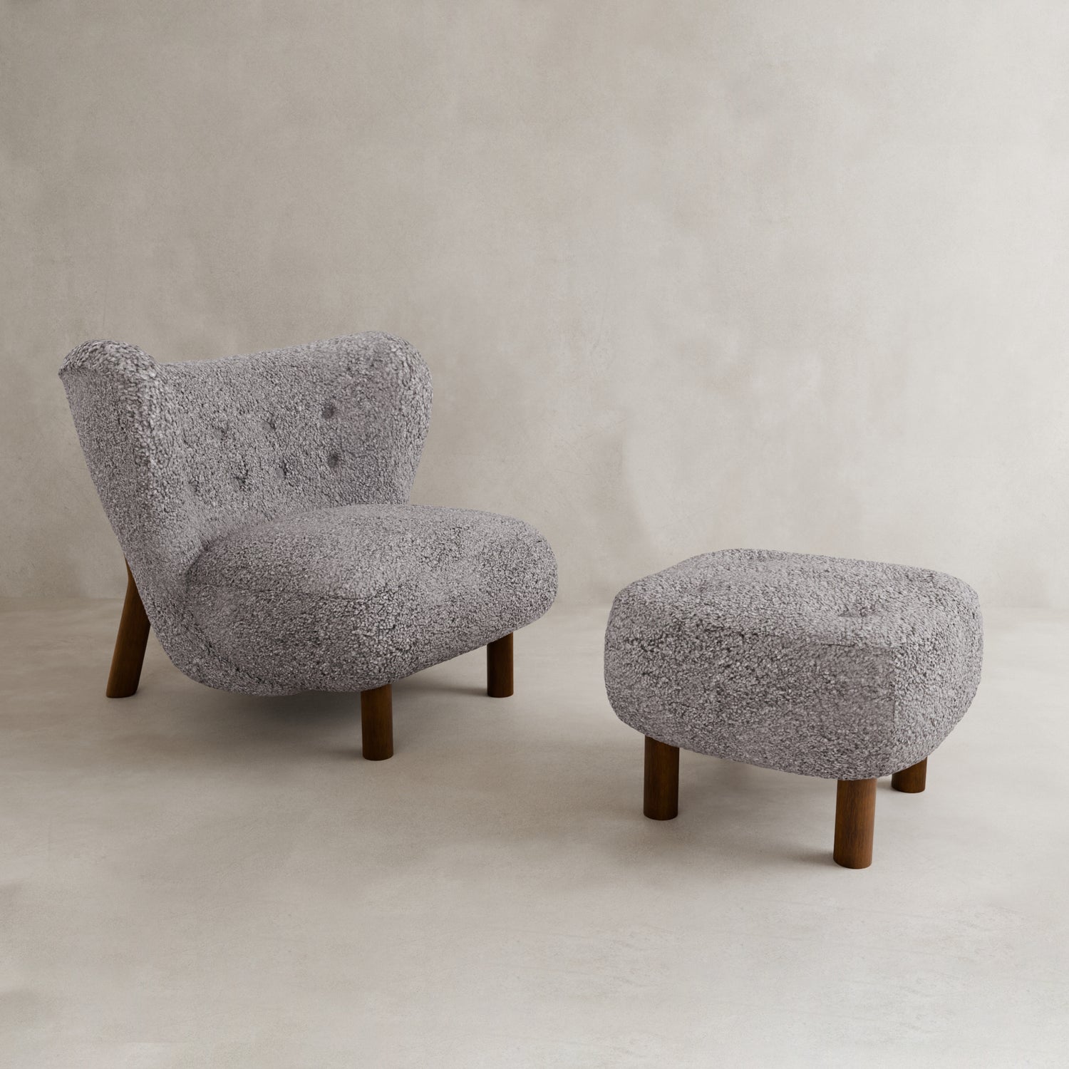 The Highgate Chair With Ottoman is a modern, light gray armchair with vegan shearling upholstery and matching ottoman, both showcasing rounded shapes, button tufting, and dark wooden legs. Set against a neutral background, it’s a true contemporary statement piece.
