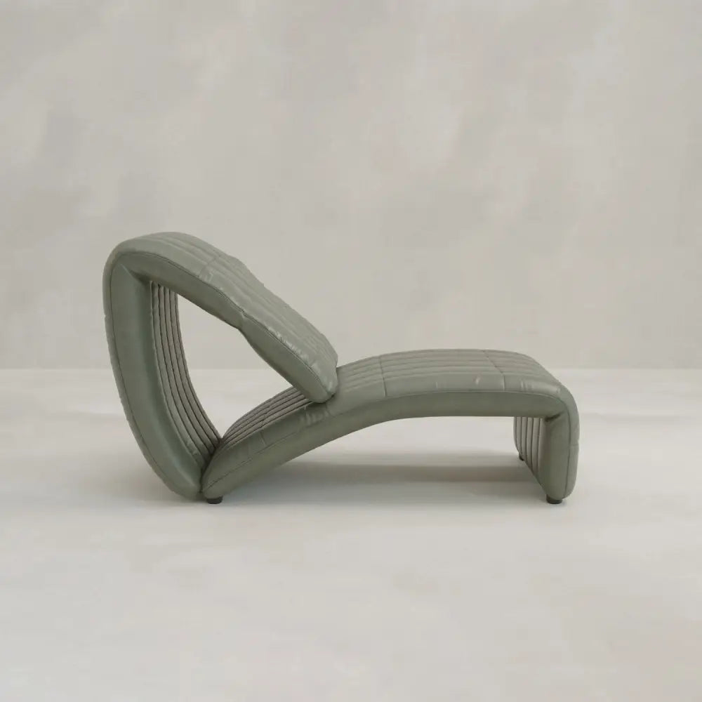 The Hillier Chair is a modern, sculptural chaise lounge with smooth green upholstery and a curved, continuous design featuring subtle reclining elements, set against a plain light gray background.