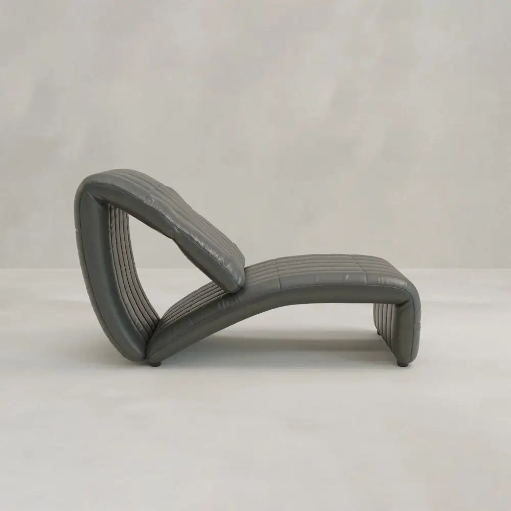 The Hillier Chair, made from premium vintage leather, boasts a modern curved design with reclining features. It’s displayed on a light floor with a plain, light grey background.
