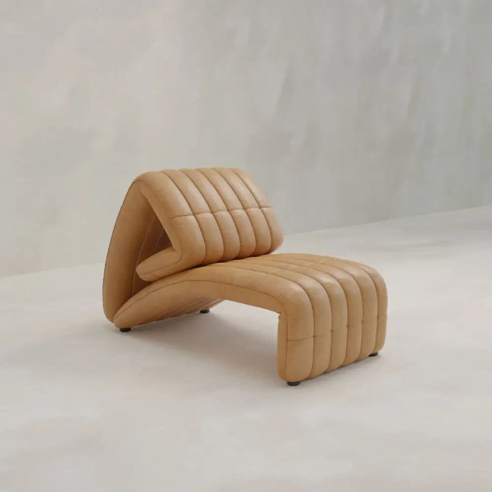 The Hillier Chair features premium vintage leather, a sculptural wavy design, and vertical stitching, shown on a light floor against a pale textured wall.