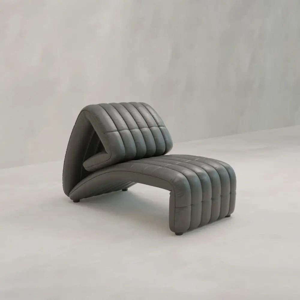 The Hillier Chair features a modern, angular zigzag design with a dark gray ribbed and cushioned surface in premium vintage leather, set against a light, minimalist background.