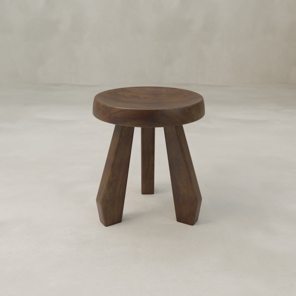 The Amara Tall Stool is a small, hand-carved wooden stool featuring a round seat and three wide, angled legs for a sturdy tripod base, shown against a plain light gray background.
