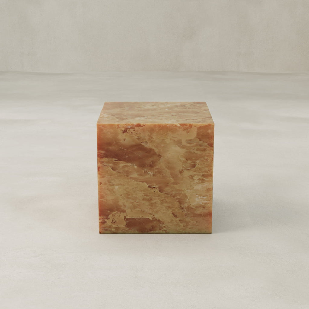 The Ambeline Onyx Plinth - Cube, crafted from polished brown, beige, and honey onyx, sits elegantly on a smooth light surface, its organic hues highlighted against a neutral background.