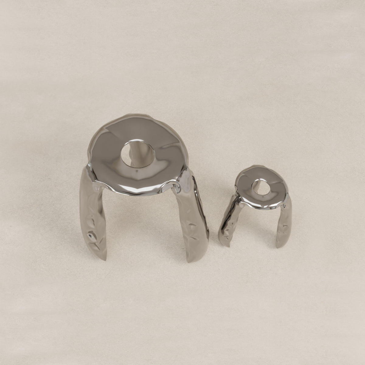 The Araknid Stool Large Rental features a metallic, three-legged sculptural design with a round top and central hole. Its sturdy build and shiny finish offer an abstract, organic look. Shown here on a textured surface alongside another stool for scale.