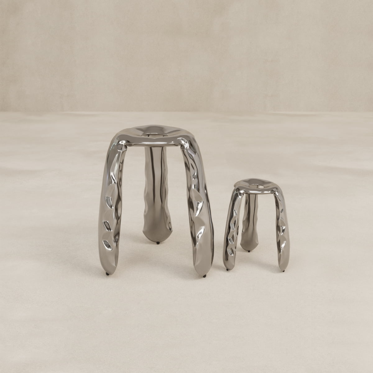 Two sturdy, reflective Araknid Stool Large Rentals with metallic finish and three twisted legs each in different heights, arranged on a smooth beige floor against a plain beige wall.