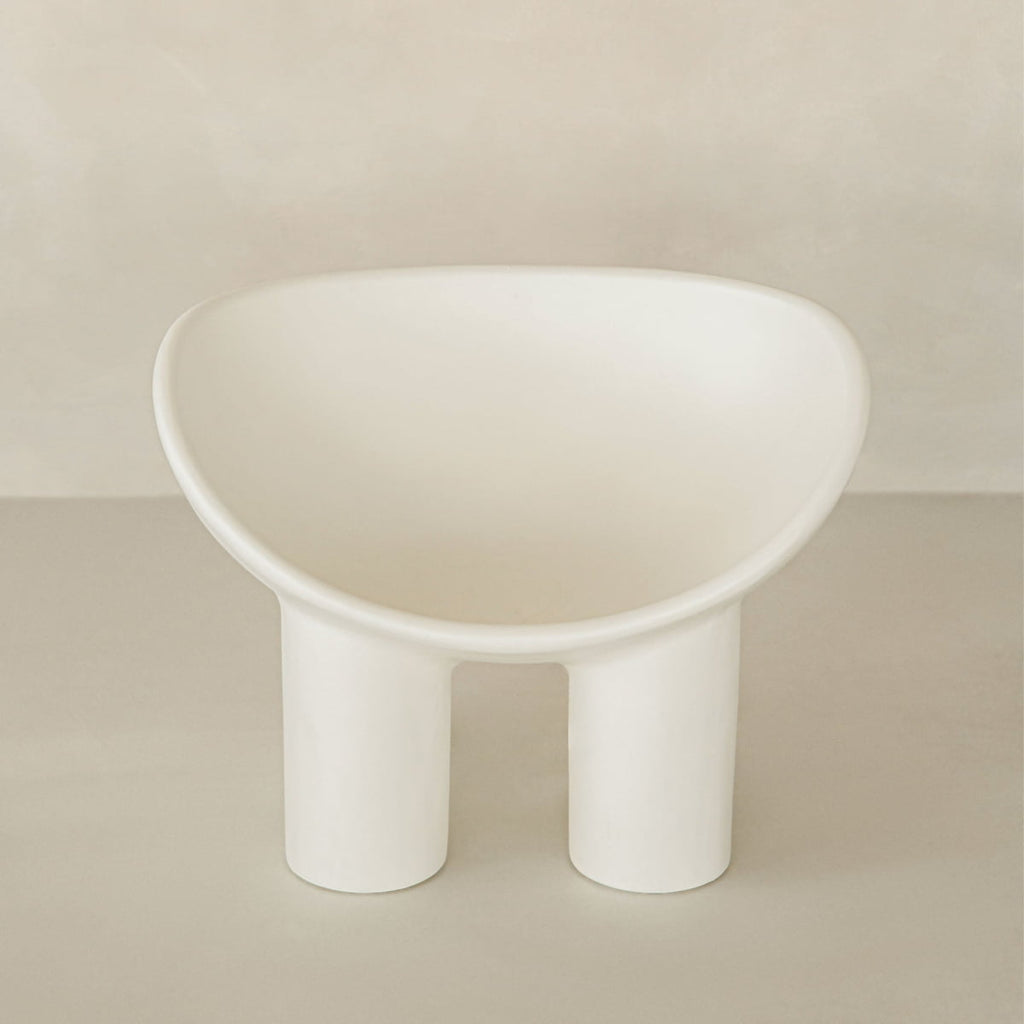 The Arrio Chair features a modern, minimalist design with a rounded seat and two thick cylindrical legs, set against a neutral beige background for an avant-garde touch.