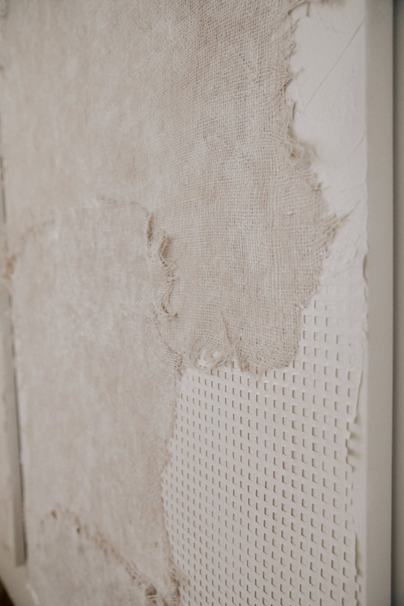 Close-up of Art By Suzette Newman canvas art, featuring textured layers of rough, torn beige fabric over a subtle grid pattern. Side angle emphasizes handmade details, rich texture, and depth.