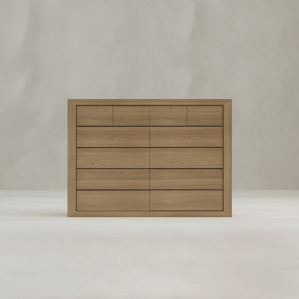 The Ashford Large Dresser, crafted from oak with a light brown finish, features three rows of four spacious drawers for ample storage and stands against a plain, light-colored background.