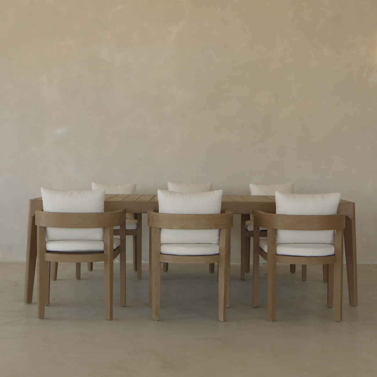 A minimalist dining setup with the Astier Outdoor Dining Table and six cushioned wooden chairs on a light floor by a beige wall brings French modernist elegance to any space.