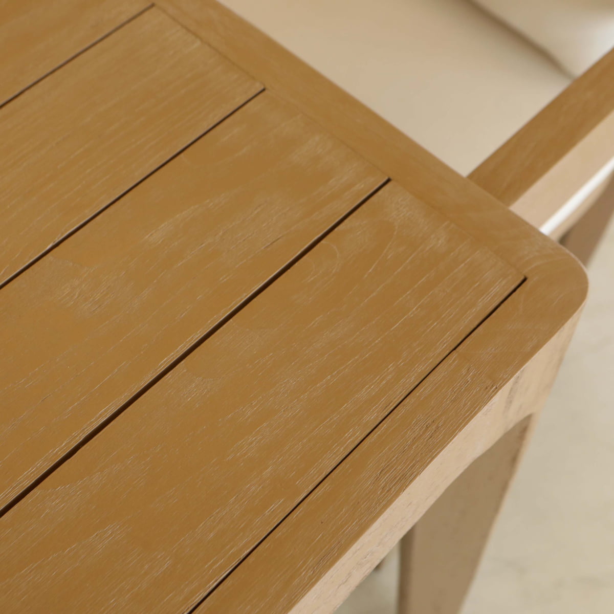 Close-up of the Astier Outdoor Dining Table Sets light wood corner with visible grain, featuring part of a matching chair and cushion—ideal for alfresco dining in a French modernist style.