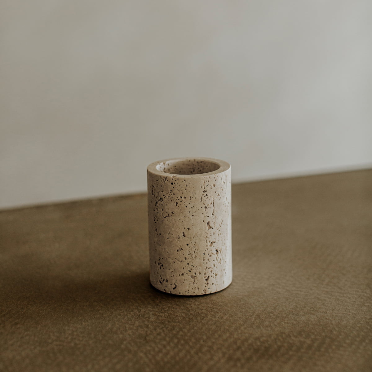 The Aurelia Goblet, featuring a beige cylindrical design with a rough, porous texture, rests on a smooth brown surface against a softly blurred neutral background to enhance your dining experience.