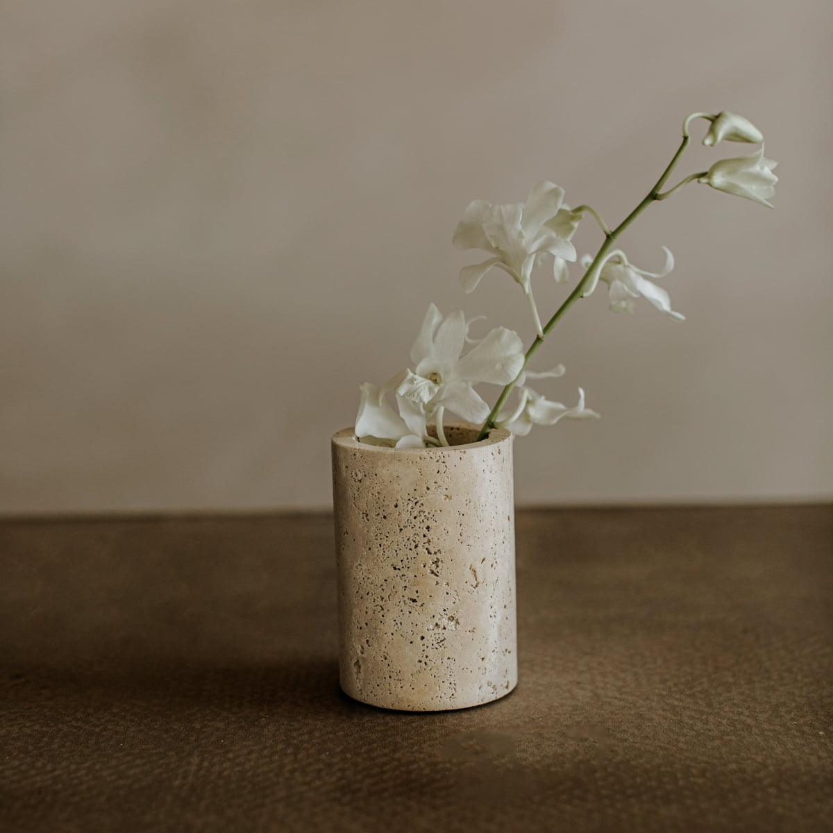 A simple white orchid stem in a textured beige vase on a brown surface echoes the timeless charm of the Aurelia Goblet, creating an elegant dining experience against a light background.