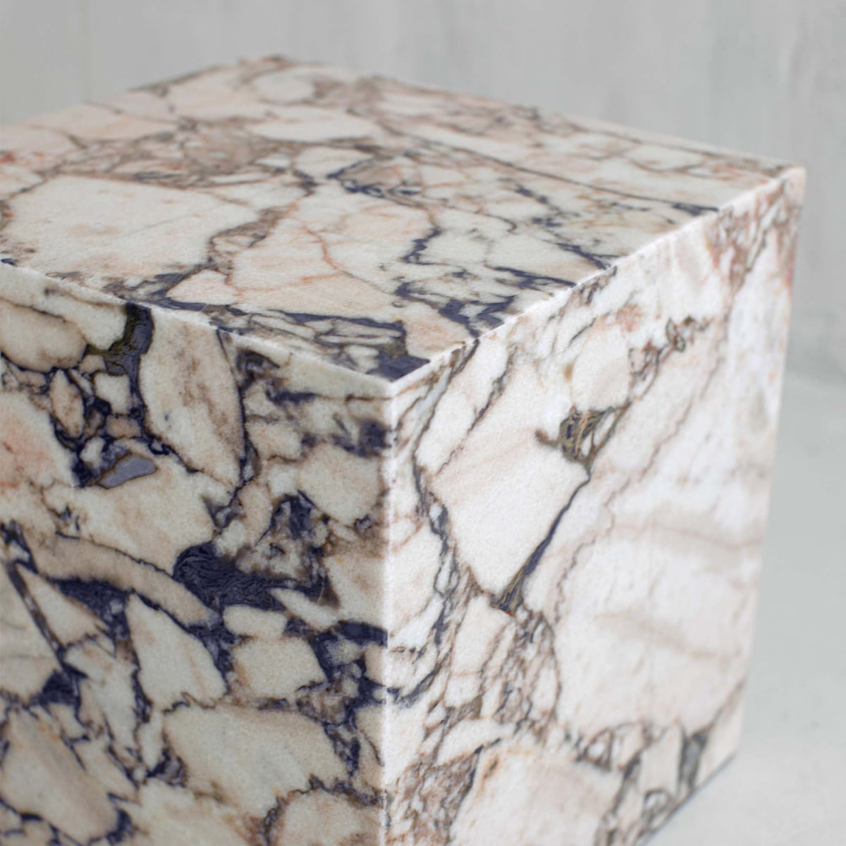 The Turkish Calacatta Plinth Cube features a close-up of its cube-shaped form, crafted from marble with white, beige, and dark gray veining on a light background.