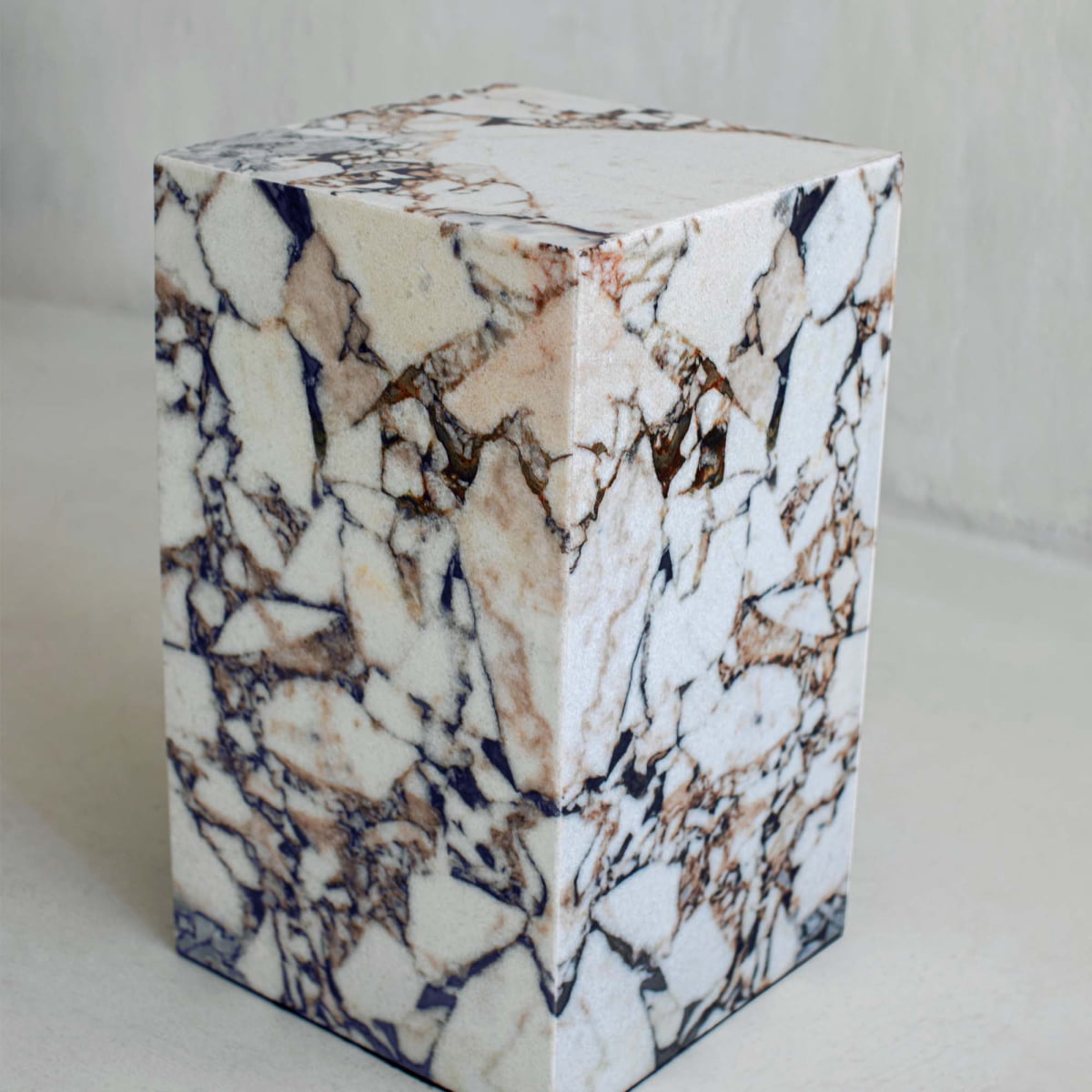 The Turkish Calacatta Plinth Tall is a rectangular block with a polished surface, showcasing a modern design and white-beige marble pattern accented by dark brown and gray veins on a light background.