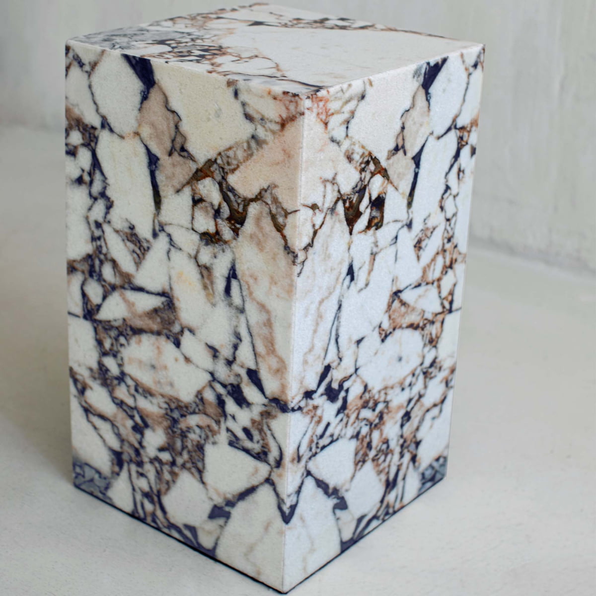 The Turkish Calacatta Plinth Tall, with a polished marble-like finish featuring white, beige, and dark gray veins, stands on a light surface against a neutral background.