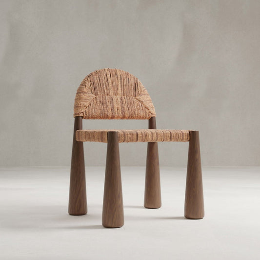 The Bardo Chair features chunky wooden legs and a seat with an arched backrest woven from natural fibers, highlighting artisanal craftsmanship against a plain light gray background.