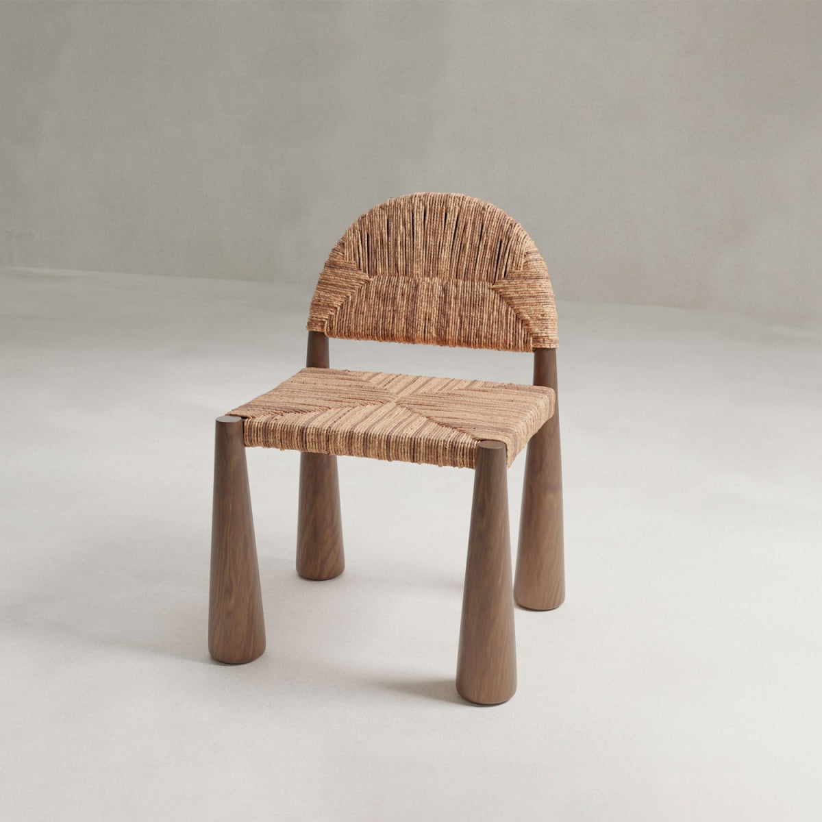 The Bardo Chair features artisanal craftsmanship with three rounded wooden legs, a woven rattan seat, and a curved backrest, showcased against a neutral, light background.