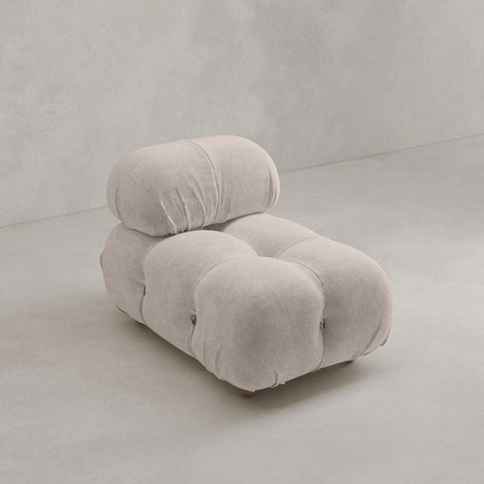 The Belmont Chair 2/3Rd Modular Sectional features a modern, light beige, tufted design with marshmallow-like curves and rounded plushness, set on a smooth gray floor against a light gray wall.