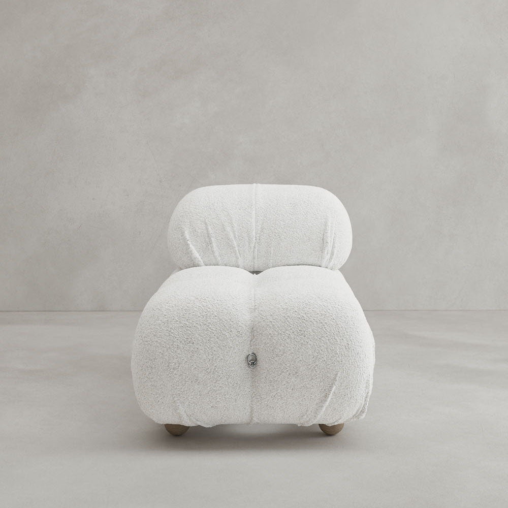 The Belmont Chair 2/3Rd Modular Sectional, a modern plush white lounge chair with tufted, rounded design and low wooden legs, features soft textured fabric and sits elegantly on a light grey floor against a plain grey wall.
