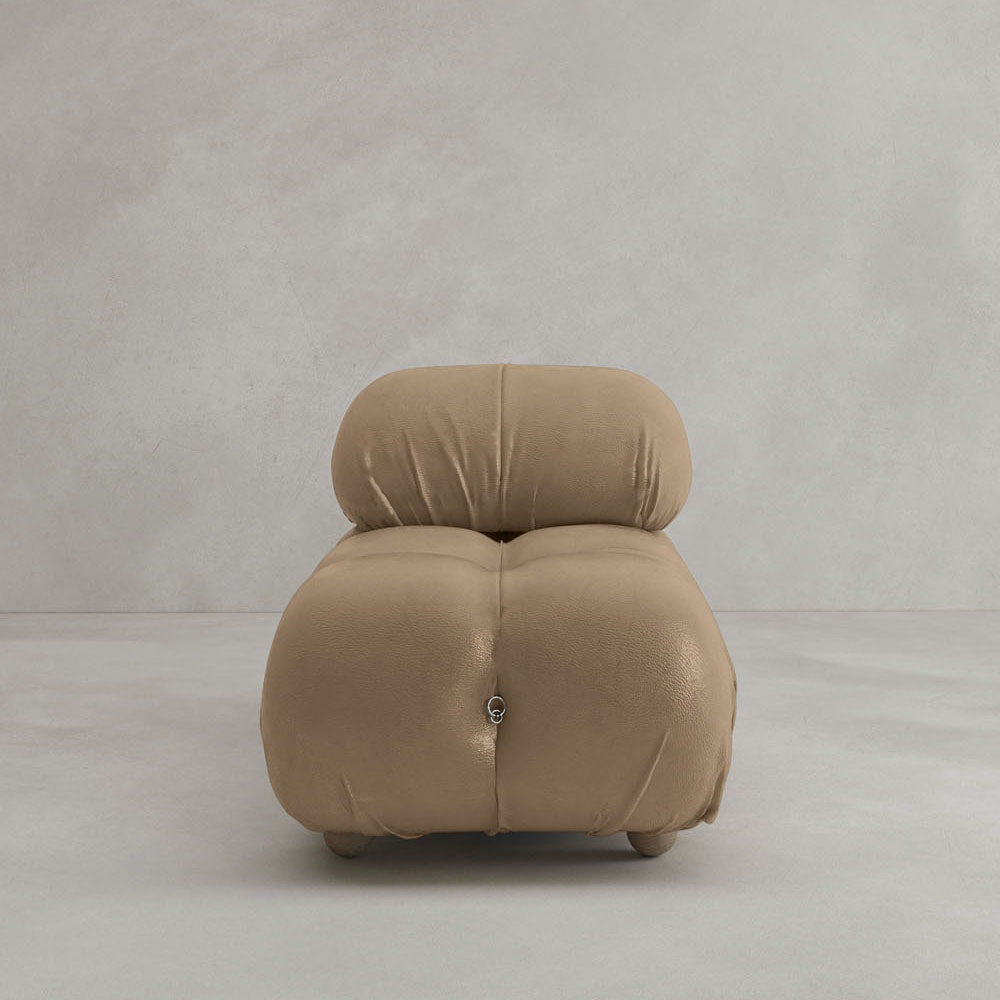 The Belmont Chair 2/3Rd Modular Sectional, featuring plush tan upholstery and rounded, tufted curves, sits on a light gray floor against a plain, textured light gray wall.