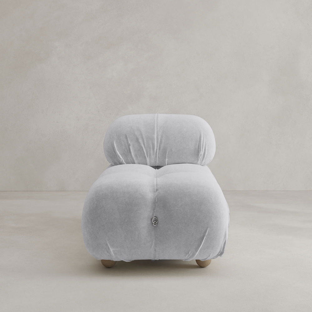 The Belmont Chair 2/3Rd Modular Sectional is a modern, armless lounge seat with marshmallow-like curves, light grey velvet upholstery, a plush tufted design, and small wooden legs against a neutral textured background.