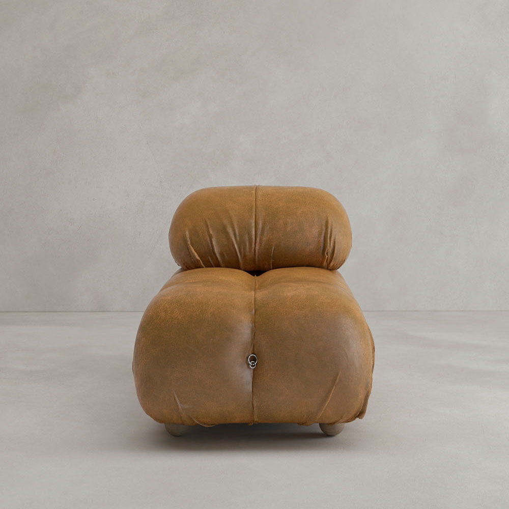 A modern Belmont Chair 2/3Rd Modular Sectional with rounded edges and tan leather upholstery, featuring tufted cushions, a modular design, and minimalist style, set against a plain light gray background.