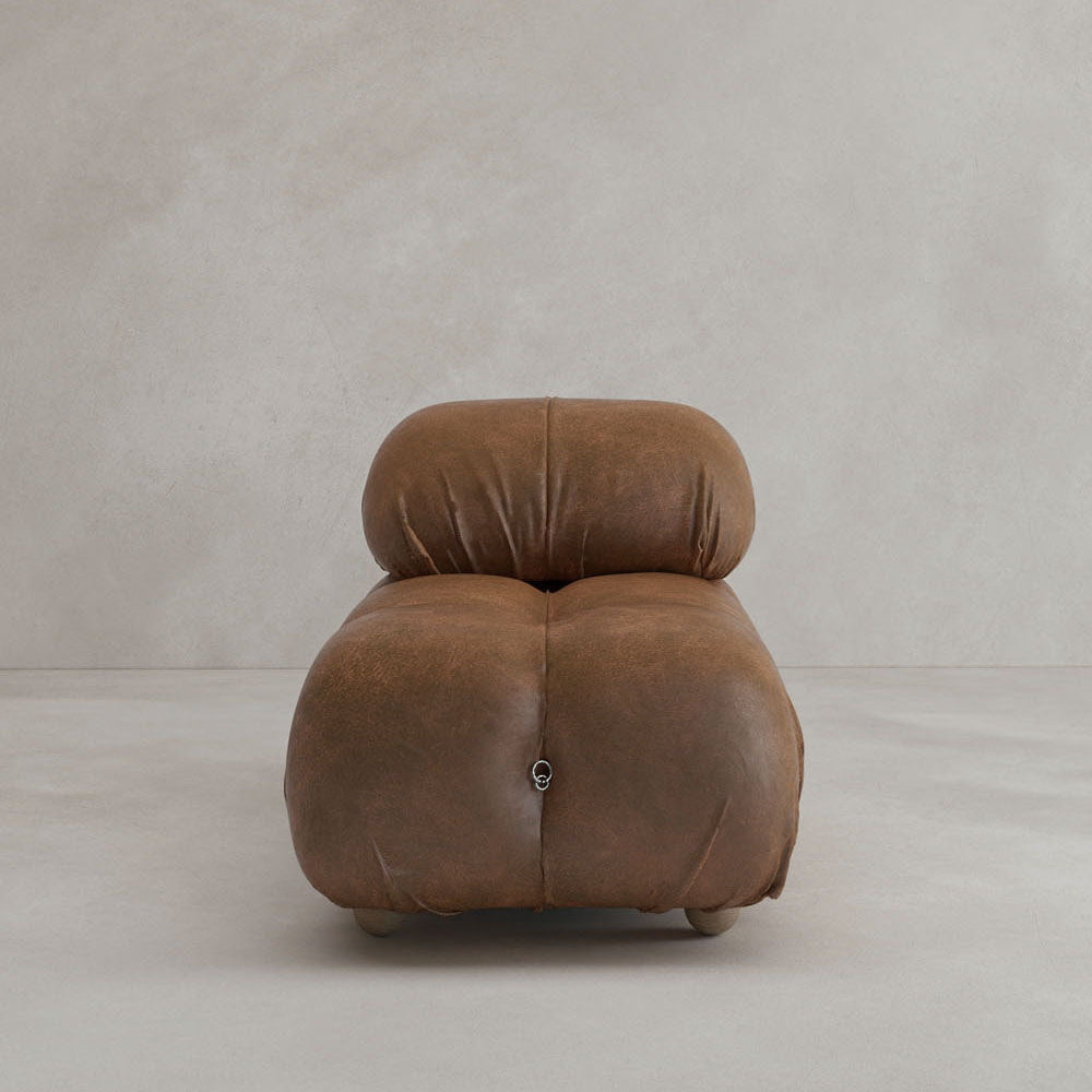 The Belmont Chair 2/3Rd Modular Sectional features marshmallow-like curves and brown leather upholstery, showcased as a single low-profile seat against a plain light gray wall and floor.