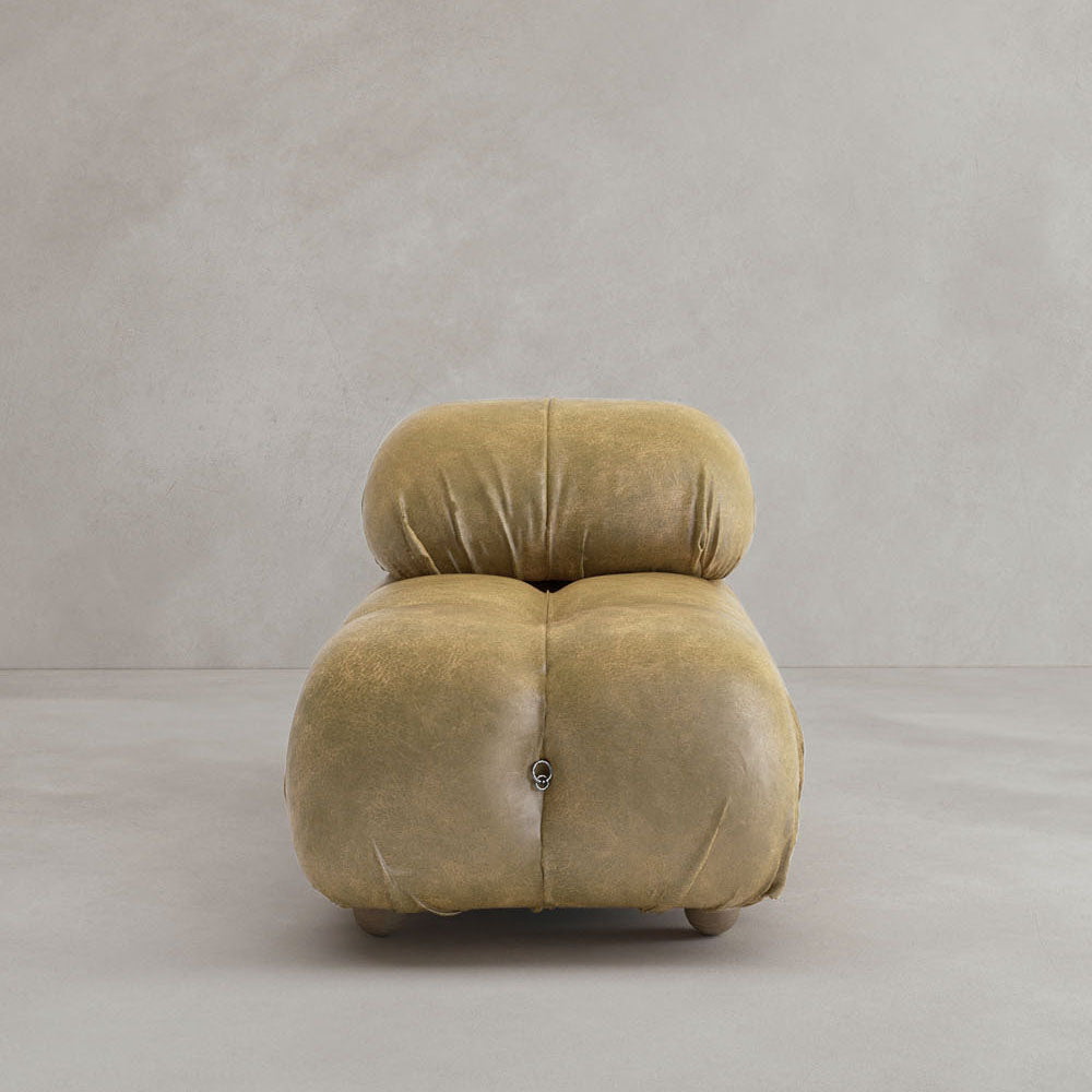 A plush, tan Belmont Chair 2/3Rd Modular Sectional with rounded edges and soft tufted design sits against a light gray wall and floor, evoking cloud-like comfort.