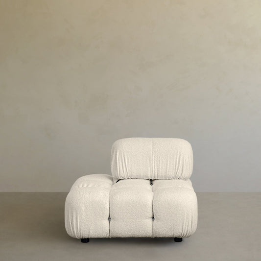The Belmont Sofa 2/3Rd Backrest features a modern, armless design with textured off-white upholstery and tufted details, offering a cloud-like comfort. It sits on a smooth gray floor against a simple beige wall.