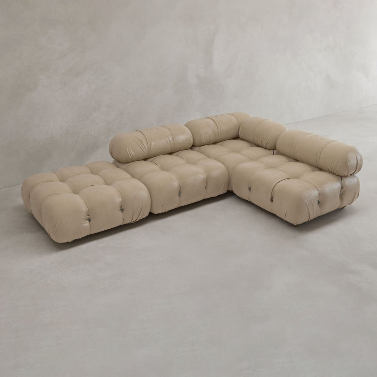 The Belmont Sofa Combination C, a modern light beige modular sectional with marshmallow-like curves and tufted cushions, sits on a smooth light gray floor against a textured off-white wall—an iconic classic of modular design.