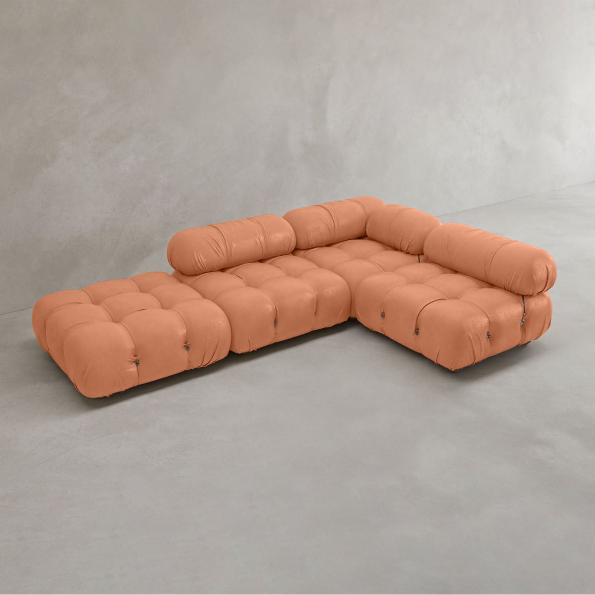 The Belmont Sofa Combination C, a modular tufted sectional with marshmallow-like curves in soft peach, is arranged in an L-shape against a plain light gray concrete wall and floor.