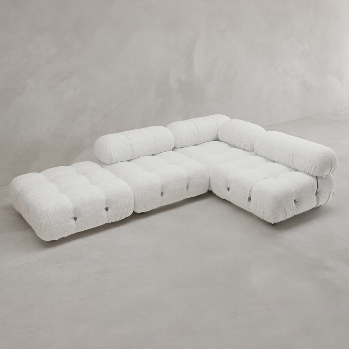 The Belmont Sofa Combination C is a modern, L-shaped modular sofa with marshmallow-like curves, tufted white upholstery, and rounded edges, displayed against a plain light grey wall and floor.