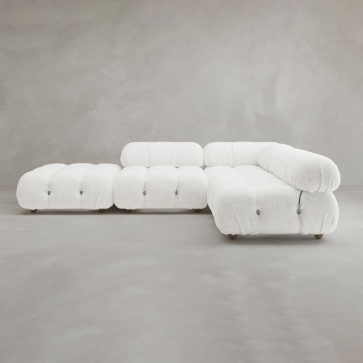 The Belmont Sofa Combination C is a modern white tufted sectional with marshmallow-like curves, rounded edges, and a matching ottoman, featuring a modular design against a plain gray background.