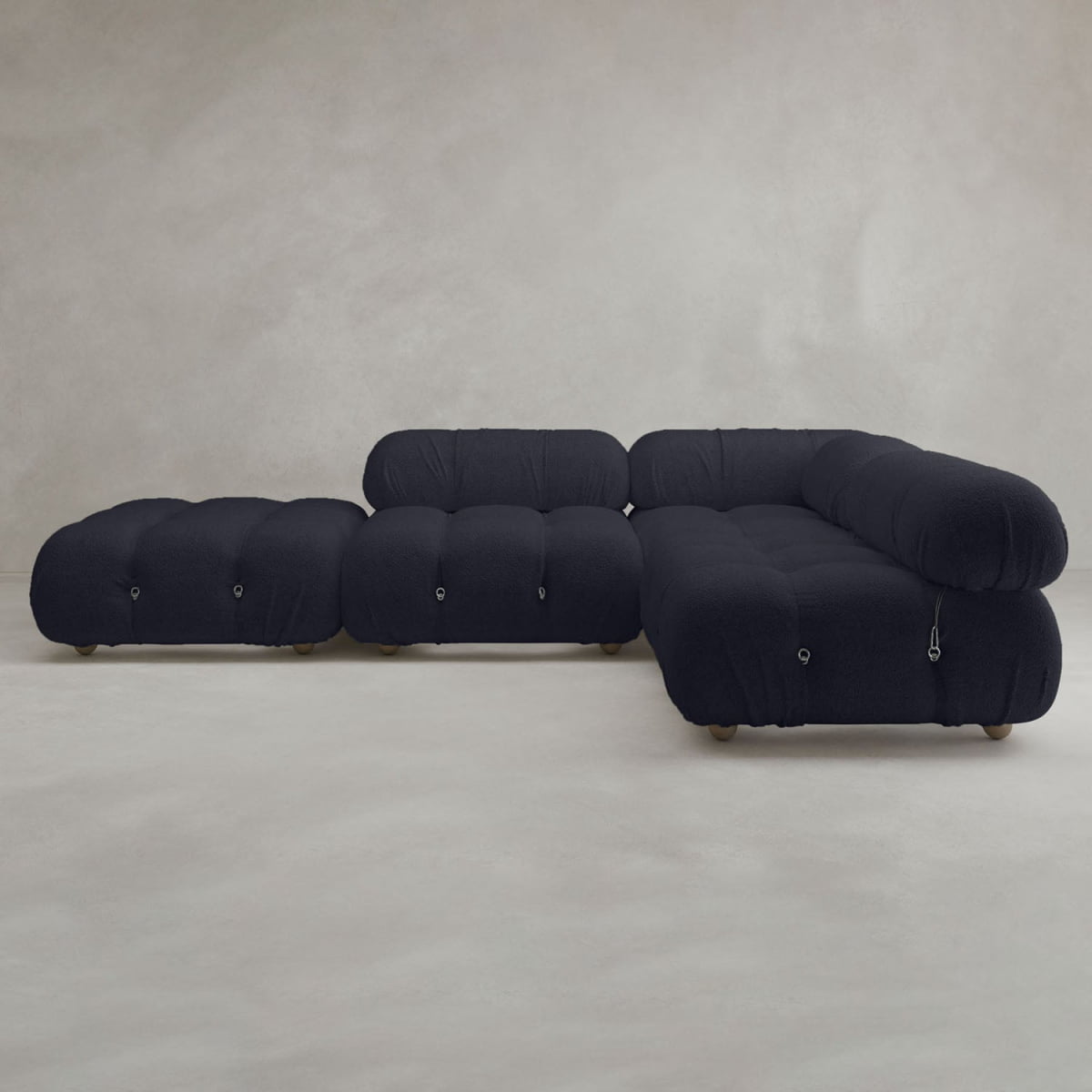 The Belmont Sofa Combination C features a modern, tufted black design with marshmallow-like curves and a low profile, set against a neutral, lightly textured backdrop in a minimalistic room.