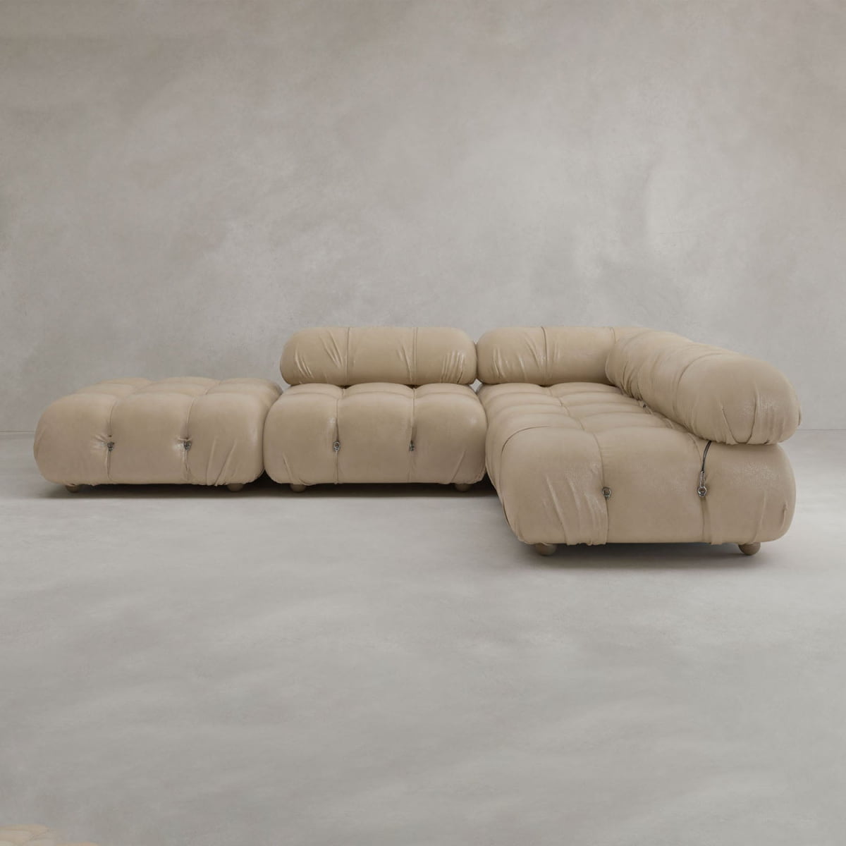 The Belmont Sofa Combination C, a modern beige sectional with tufted cushions and rounded edges, sits on a smooth light gray floor against a neutral gray wall.
