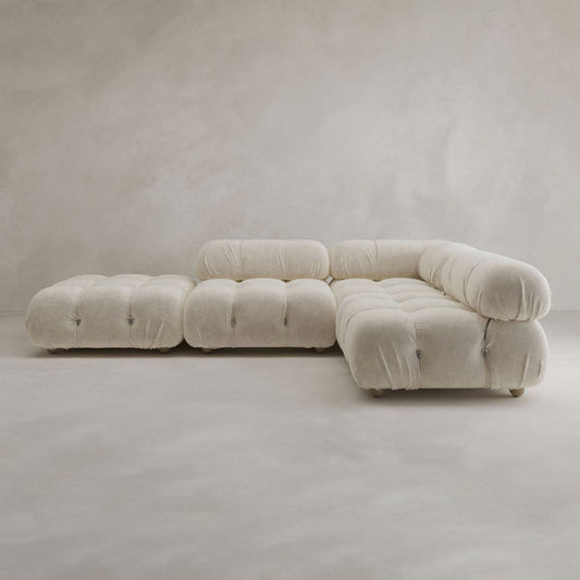 The Belmont Sofa Combination C is a modern modular sectional with marshmallow-like curves, tufted rounded cushions, and a matching ottoman, all upholstered in light beige fabric and set against a plain, light background.