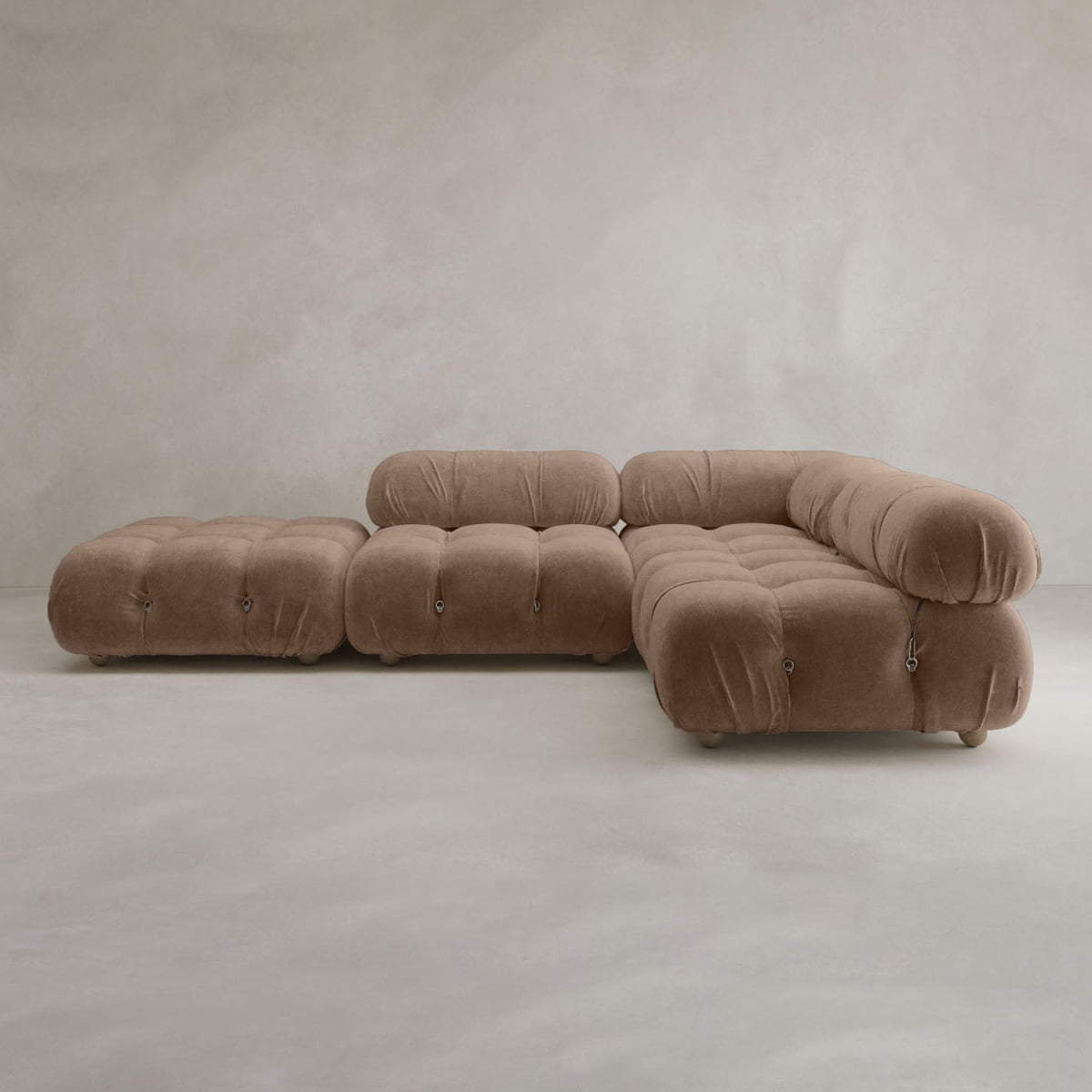 The Belmont Sofa Combination C—a modular, tufted brown sofa with plush, marshmallow-like curves—rests against a plain, light gray textured wall and floor.
