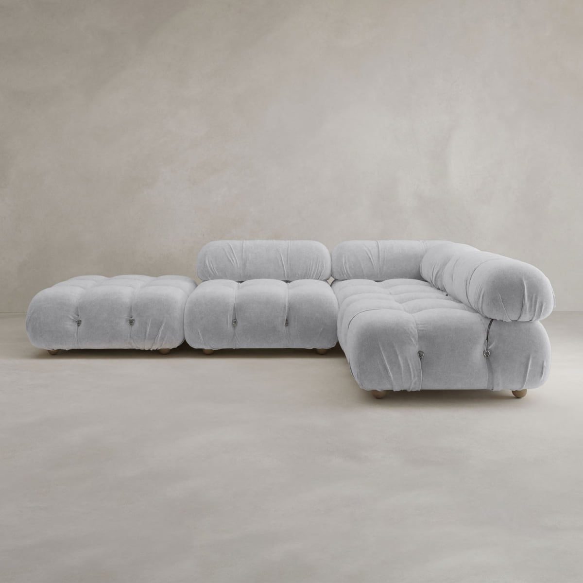 The Belmont Sofa Combination C, with its light gray hue, modern design, plush tufted cushions, and soft curves, sits on a neutral floor against a beige textured wall.