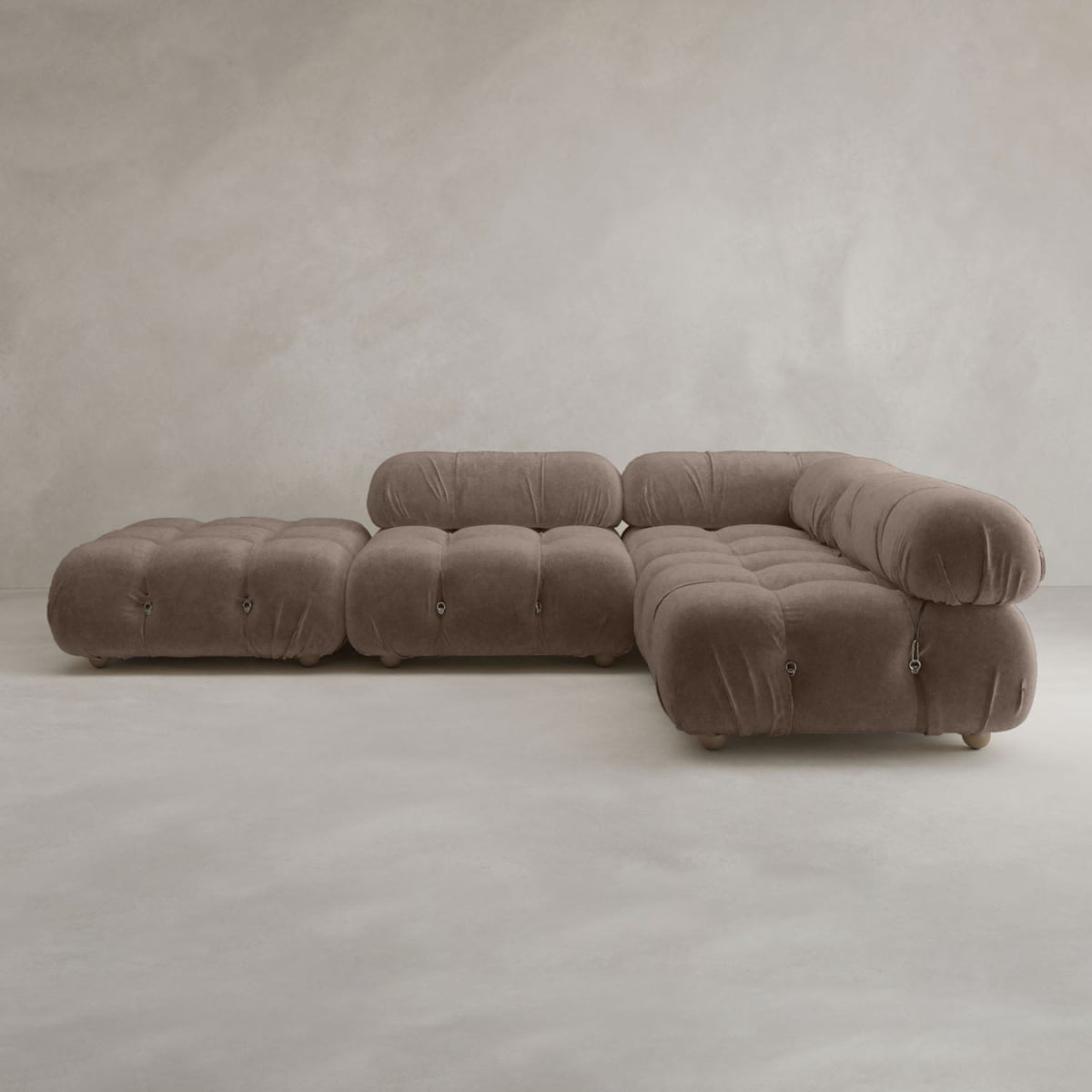 The Belmont Sofa Combination C is a modern sectional with marshmallow-like curves, deep tufting, a matching ottoman, and soft brown upholstery, set against a neutral textured wall and floor.