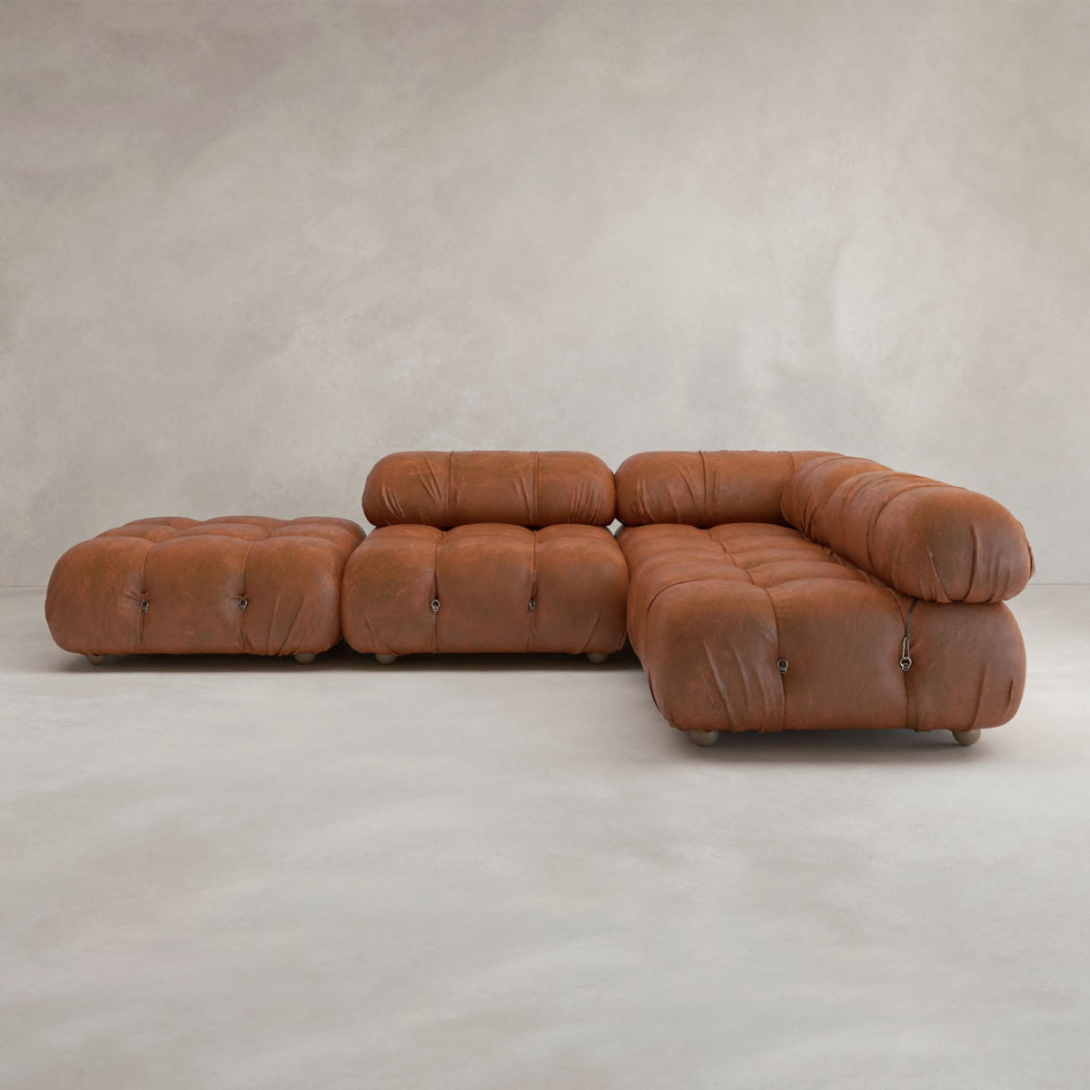 The Belmont Sofa Combination C features brown leather, tufted cushions, and marshmallow-like curves, arranged on a light neutral floor against a textured beige wall—an iconic classic of modular design.