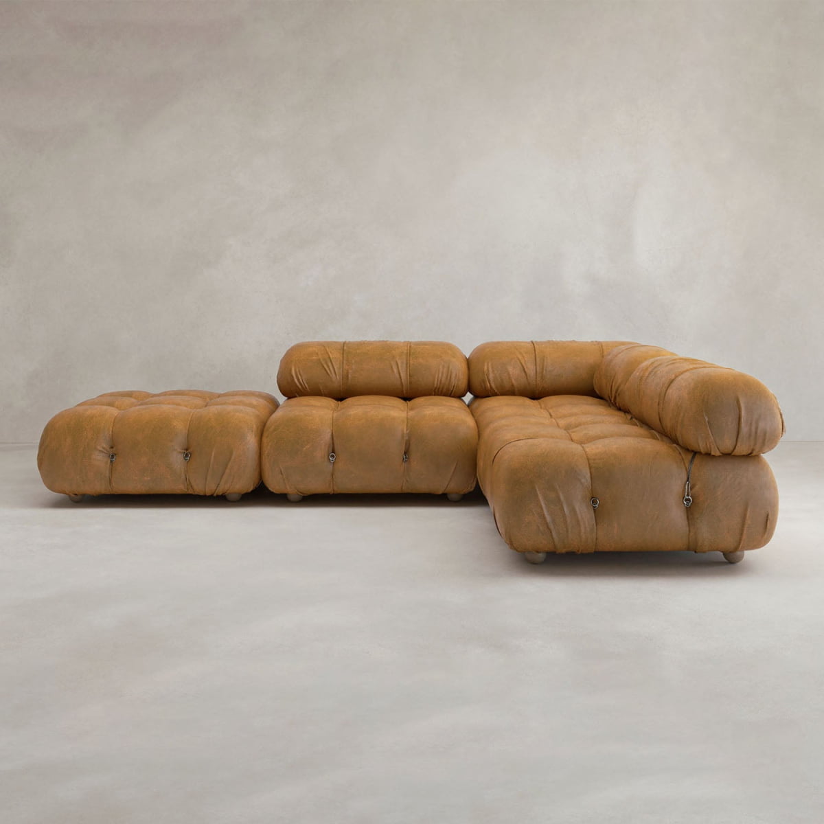 The Belmont Sofa Combination C is a modern, modular tan leather sofa with tufted cushions, rounded edges, and marshmallow-like curves, arranged in an L-shape with an ottoman beside it against a light background.