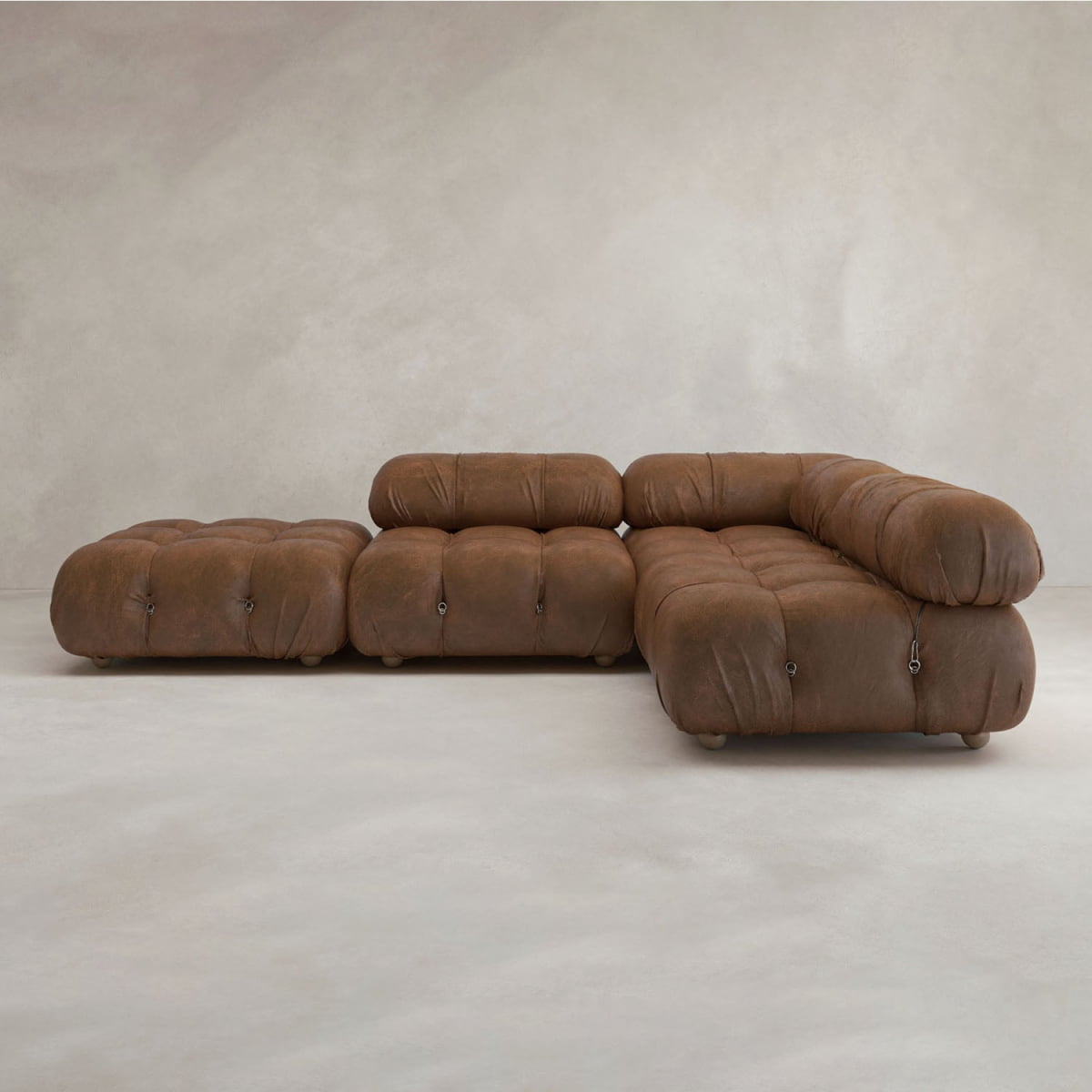 The Belmont Sofa Combination C is a modular brown leather sectional with plush, tufted cushions and marshmallow-like curves, featuring an attached chaise lounge and set against a neutral, textured background.