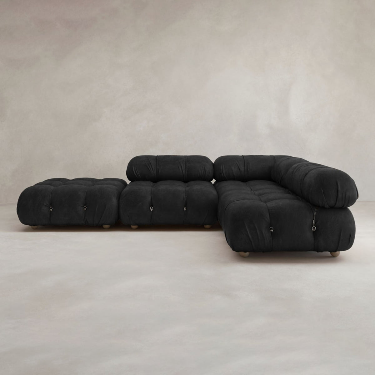 The Belmont Sofa Combination C, featuring a modular design with tufted cushions and black upholstery, is placed on a light floor against a neutral textured wall.