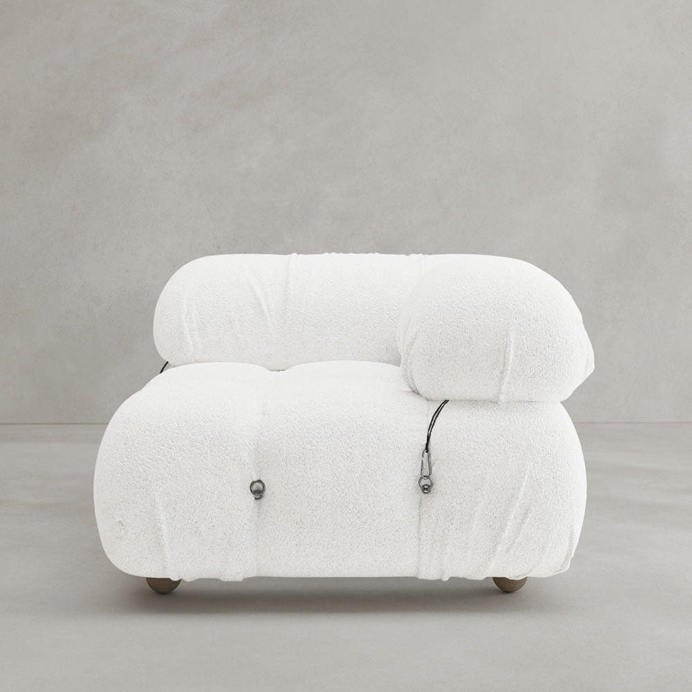The Belmont Sofa Left Armrest is a modern, armless white lounge chair with plush textured fabric, rounded cushions, visible black cord details, and a modular design; displayed on a plain light gray background.