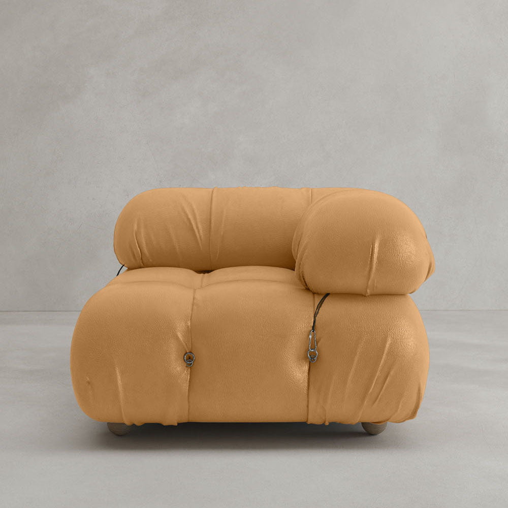 The Belmont Sofa Left Armrest features a modern tan design with plush, overstuffed cushions and visible black fastening cords, evoking a modular aesthetic against a plain light gray background.