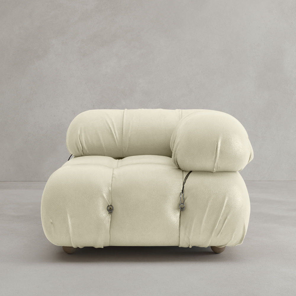 A modern, plush white Belmont Sofa Left Armrest with a rounded, tufted design and metal fasteners, featuring modular elements, set against a plain light gray wall and floor.